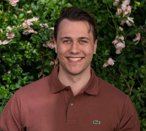 A portrait photo of AI researcher Sebastian Wind in front of a rose bush.