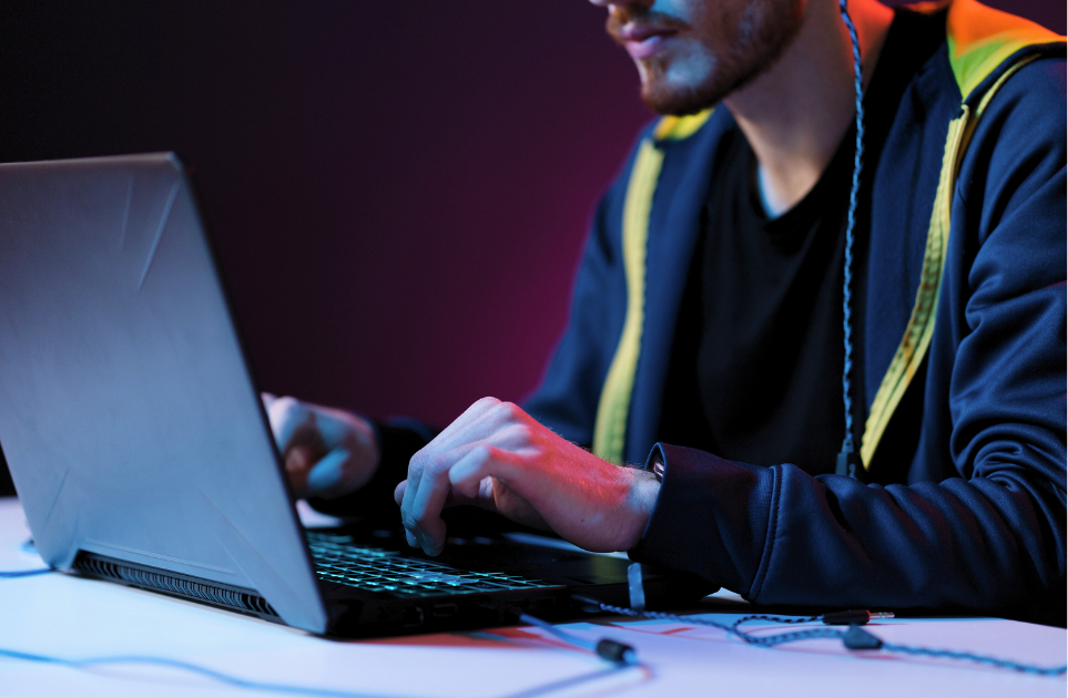 A young man is typing on a laptop in a dark room.